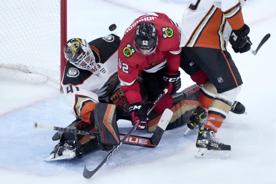 Chicago Blackhawks' Reese Johnson (52) falls between Anaheim Ducks goaltender Anthony Stolarz (41) and Simon Benoit as the puck bounces off the wall behind them during the third period of an NHL hockey game Tuesday, Feb. 7, 2023, in Chicago. The Ducks won in overtime 3-2. (AP Photo/Charles Rex Arbogast)