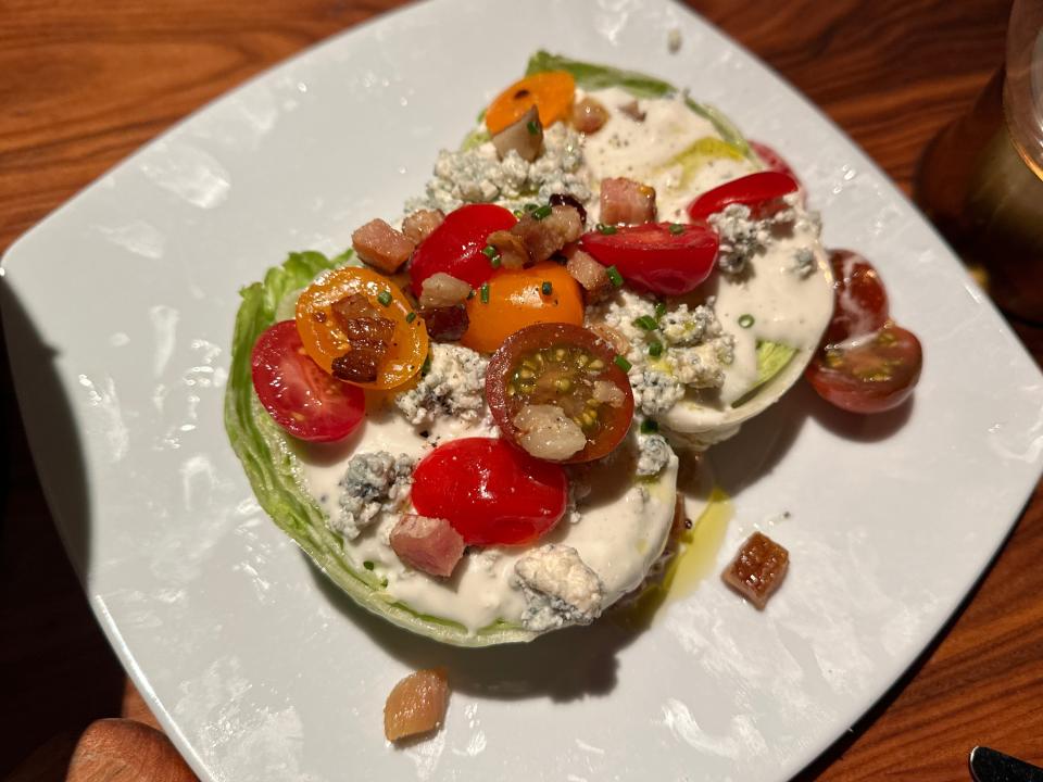 A wedge salad with halved cherry tomatoes, halves of a lettuce head, and a white dressing dripping off the lettuce on a square plate