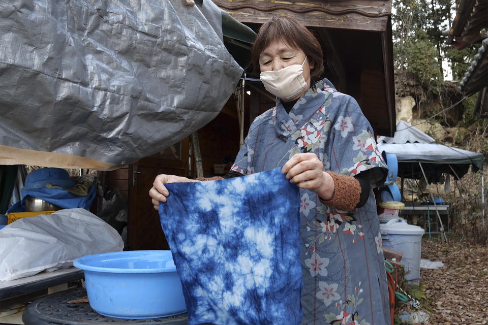 In this image from video, Yoshiko Ogura, 73, holds up a handkerchief dyed without using any chemical substances in front of her studio in Minamisoma, Fukushima Prefecture, northeastern Japan, on Feb. 20, 2021. After the Fukushima nuclear plant disaster a decade ago, nearby farmers weren't allowed to grow crops for two years because of radiation. After the restriction was lifted, two farmers in the town of Minamisoma found an unusual way to rebuild their lives and help their destroyed community. Kiyoko Mori and Ogura planted indigo and soon began dying fabric with dye produced from the plants. (AP Photo/Chisato Tanaka)