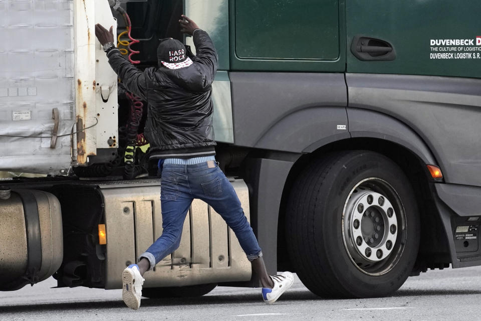 A migrant jumps on a truck to try to cross the tunnel heading to the UK, in Calais, northern France, Thursday, Oct. 14, 2021. In a dangerous and potentially deadly practice, he is trying to get through the heavily policed tunnel linking the two countries by hiding on a truck. (AP Photo/Christophe Ena)