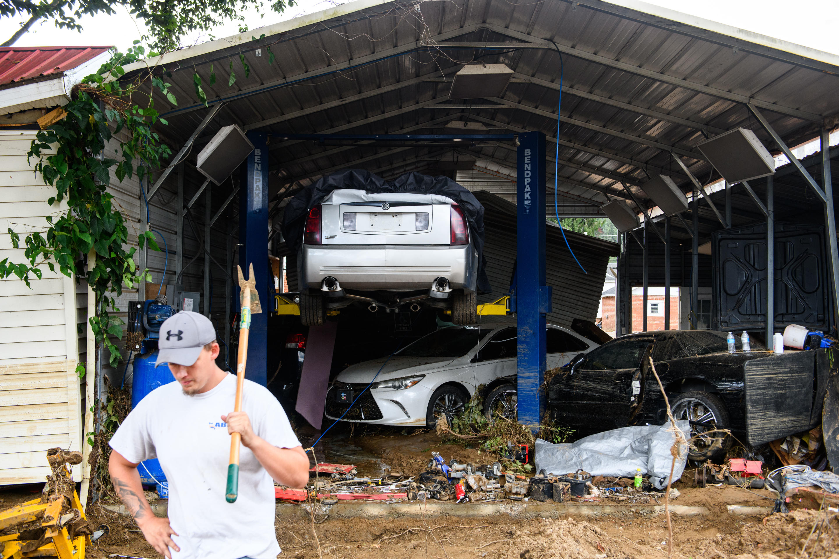 A man stands near vehicles damaged by floods and debris.