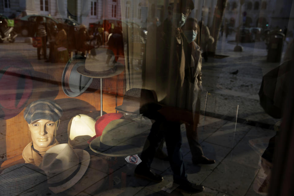 A couple wearing face masks are reflected on the window of a hat shop in downtown Lisbon, Wednesday, Dec. 2, 2020. (AP Photo/Armando Franca)
