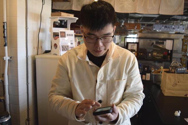Coffee shop owner Chiu Sih-chi looks at his cellphone at his shop Z.O. coffee in Nangan, part of Matsu Islands, Taiwan on Sunday, March 5, 2023. Chiu said the recent internet outage made it difficult to book a hospital appointment for his toddler. Thousands of residents of Taiwan's outlying islands near the Chinese coast have been without the internet for the past month. Chunghwa Telecom, Taiwan's largest service provider and owner of the two submarines cables that serve Matsu islands, says Chinese vessels cut them. (AP Photo/Huizhong Wu)