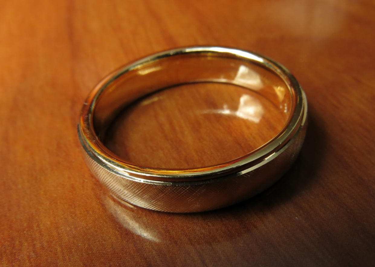  A gold wedding band on a wooden table. 