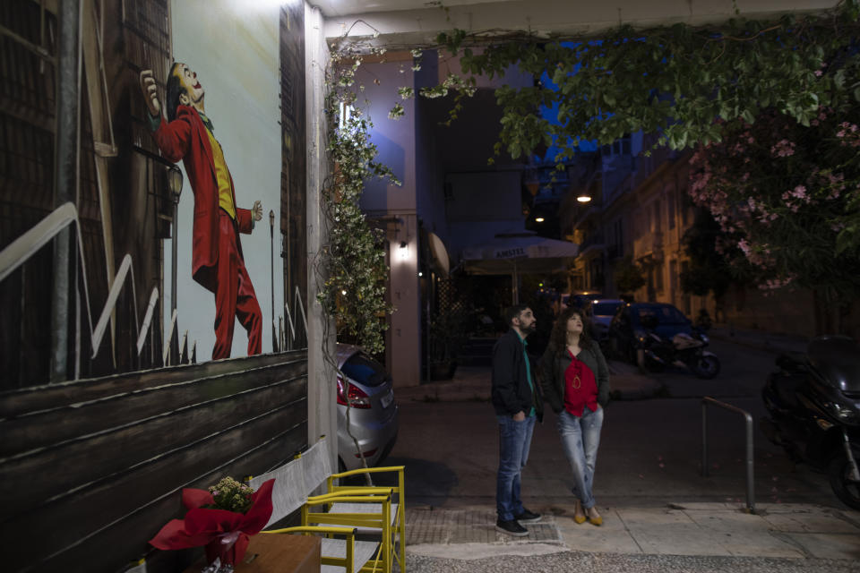 In this Tuesday June 2 , 2020 photo moviegoers stand next to a painting by Pavlos Karakasidis showing the 2019 movie 'Joker' at the Panathinea open-air cinema, in central Athens. (AP Photo/Petros Giannakouris)