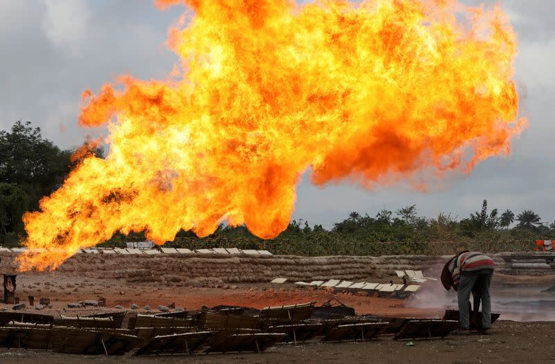 A man sets a wooden tray of tapioca on the ground close to a gas flaring furnace at a flow station in Ughelli, Delta State