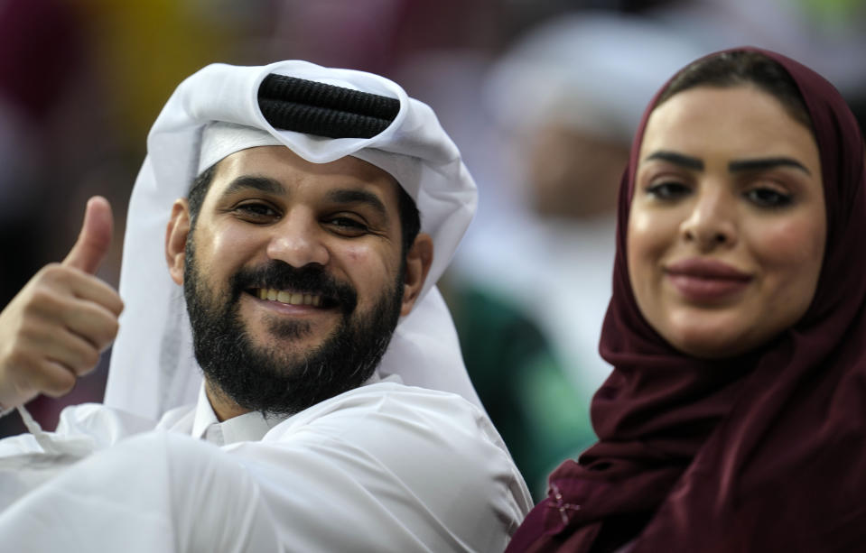 A couple on the tribune smiles to the camera prior the World Cup, group A soccer match between Qatar and Ecuador at the Al Bayt Stadium in Doha, Sunday, Nov. 20, 2022. (AP Photo/Natacha Pisarenko)