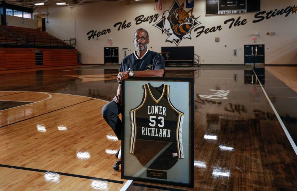 Lower Richland head basketball coach Jo Jo English played ball with Stanley Roberts on the 1987 and 1988 championship teams. He poses with Stanley Robert’s retired jersey that hangs in the school. Both English and Roberts went on to play in the NBA.