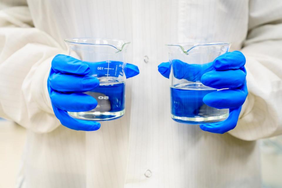 PHOTO: A person in a lab coat holding two beakers with clear liquids. (STOCK PHOTO/Getty Images)