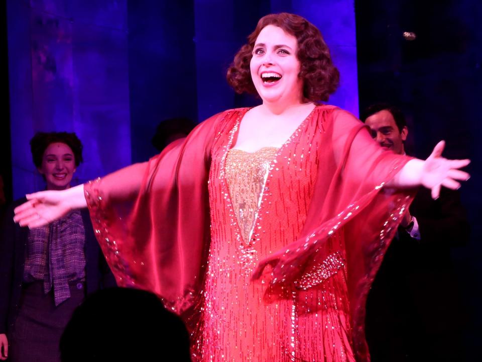 Beanie Feldstein, in a sparkling red gown, smiles onstage with arms outstretched during the curtain call for "Funny Girl" in March 2022.