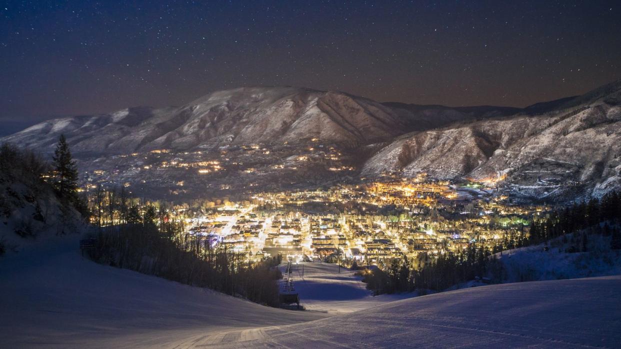 Illuminated cityscape by mountains seen from ski slope at night