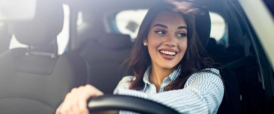 Happy woman driving a car and smiling. Cute young success happy brunette woman is driving a car. Portrait of happy female driver steering car with safety belt