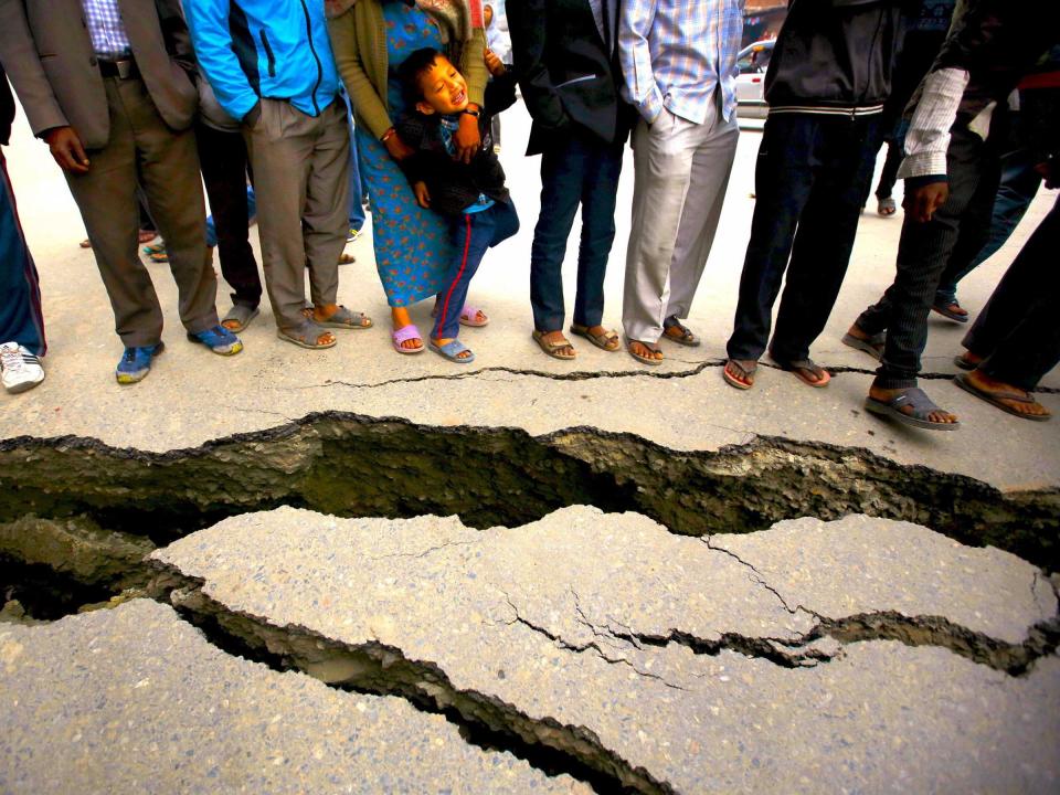 People gather near the cracks on the road caused by an earthquake in Bhaktapur, Nepal April 26, 2015. Rescuers dug with their bare hands and bodies piled up in Nepal on Sunday after an earthquake devastated the heavily crowded Kathmandu valley, killing at least 1,900, and triggered a deadly avalanche on Mount Everest.