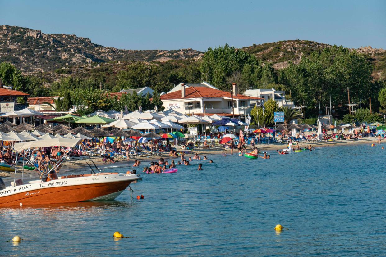 Crowd of tourists at the popular and famous beach of Kalamitsi located on the southern tip of Sithonia peninsula in Chalkidiki in Northern Greece. People have fun at the beach in Greece as they are relaxing under the shadow of the umbrellas, snorkeling, scuba diving, swimming in the tropical exotic crystal clear clean waters, doing water sports, renting boats, having a drink at the beach bars or sunbathing on the golden sand and enjoying beach life under the sunny blue sky. There is a little island also located close to the shore. 
The local government is adding new safety measures such as social distancing, changing the working hours, obligatory facemask usage etc against the spread of the Coronavirus Covid-19 Pandemic outbreak after relaxing the lockdown, travel and traffic ban, quarantine a few weeks ago, trying to relaunch the tourism season, but recently the number of cases began increasing in Greece, especially to locations near summer holiday destinations, resorts, beach bars, travel locations, night club party etc involving mostly tourists and younger people. The beachbars in Halkidiki infected a large number of people the previous days. August 14, 2020 - Halkidiki, Greece (Photo by Nicolas Economou/NurPhoto via Getty Images)