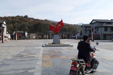 A man and a child ride a motorcycle on a plaza with a statue featuring the Chinese Communist Party emblem, in Shazhou village, Rucheng county, Hunan province, China December 3, 2018. Picture taken December 3, 2018. REUTERS/Shu Zhang