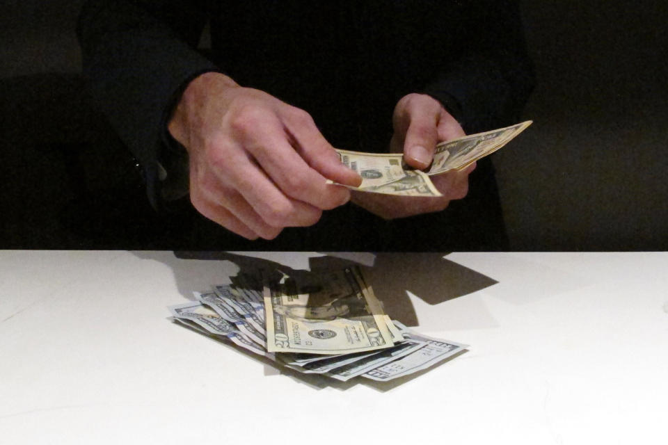 FILE — In this June 27, 2019 file photo, a clerk counts money at a sportbook, in Atlantic City, N.J. New Jersey's top gambling regulator is threatening to fine sports books operating in his state that ask customers to cancel requests to cash out money from their accounts, saying the practice is ongoing and "unacceptable." (AP Photo/Wayne Parry, File)