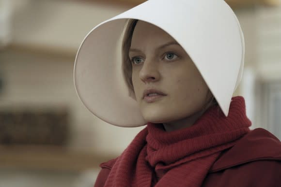 A woman dressed in red, wearing a long, white hat in a scene from The Handmaid's Tale.