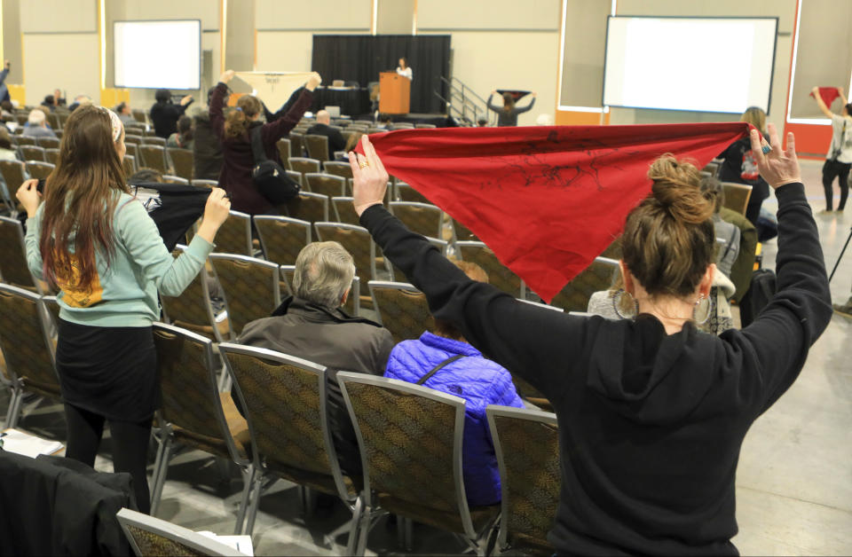 Protesters hold up flags during a public hearing on a draft environmental plan on proposed petroleum leasing within Alaska's Arctic National Wildlife Refuge on Monday, Feb. 11, 2019, in Anchorage, Alaska. Congress in December 2017 approved a tax bill that requires oil and gas lease sales in the refuge to raise revenue for a tax cut backed by President Donald Trump. (AP Photo/Dan Joling)