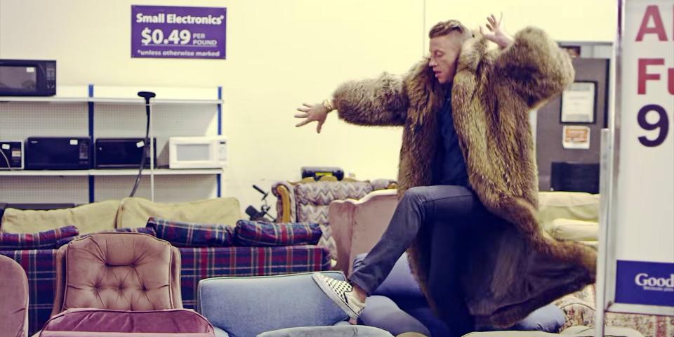Macklemore wearing a large fur coat in a thrift shop.
