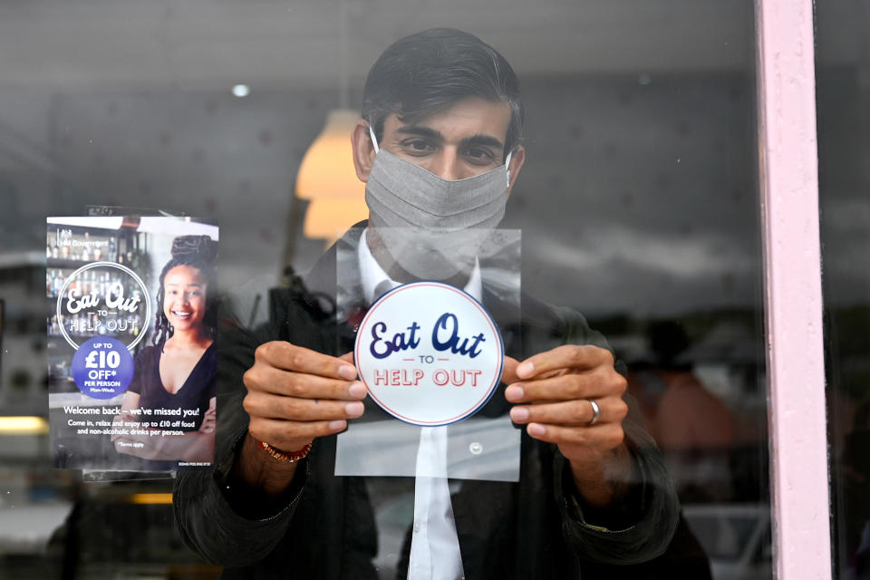 Chancellor of the Exchequer Rishi Sunak places an Eat Out to Help Out sticker in the window of a business during a visit to Rothesay on the Isle of Bute, Scotland.