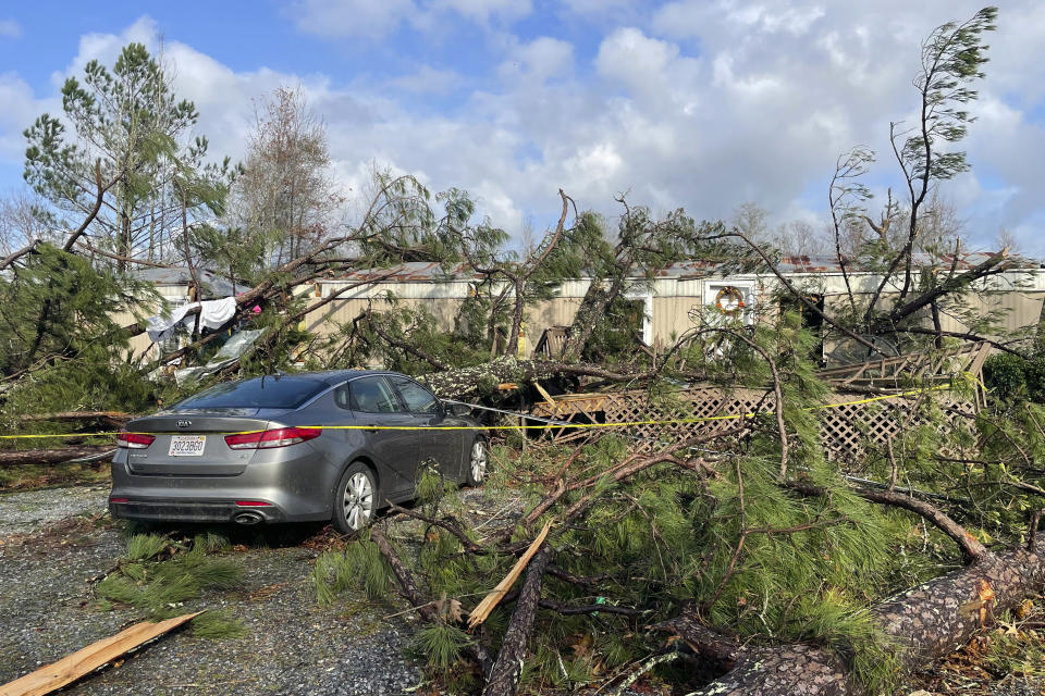 A damaged mobile home where two people died, with fallen trees all around.