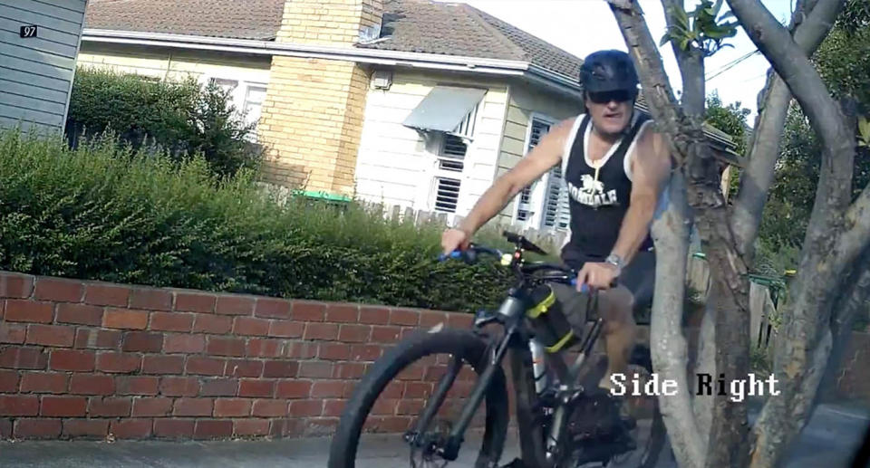 The man is seen riding a bicycle and wearing a black Lonsdale vest.