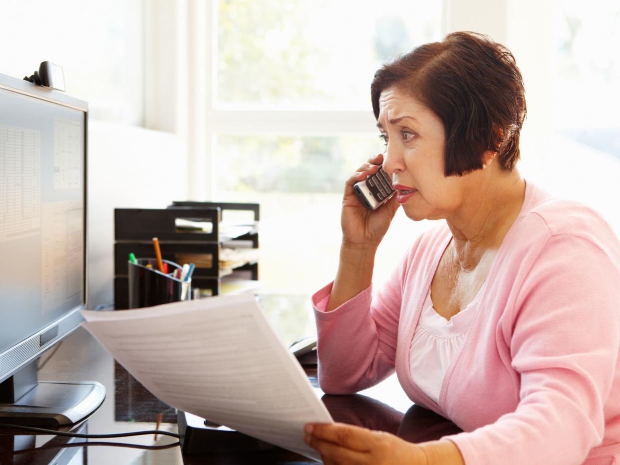 Senior Hispanic woman working on computer at home looking worried on the phone