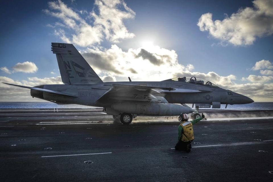 A person gives a thumbs up on the flight deck next to a fighter jet