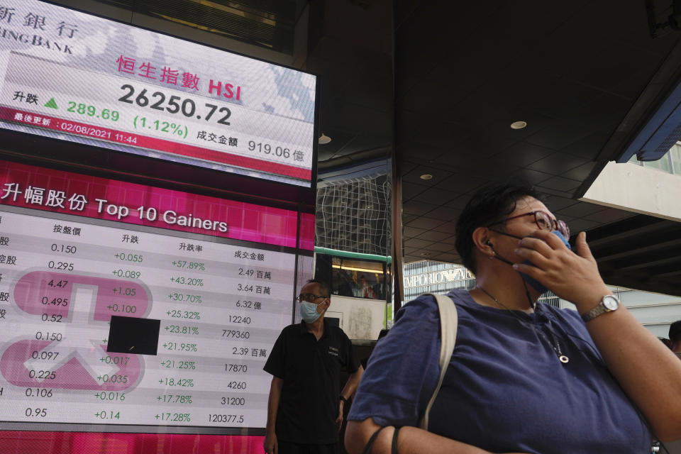 A woman walks past a bank's electronic board showing the Hong Kong share index at Hong Kong Stock Exchange in Hong Kong Monday, Aug. 2, 2021. Asian stocks have started the week higher, even as China reported a slowdown in manufacturing activity and countries in the region continue to be hammered by the delta variant. (AP Photo/Vincent Yu)
