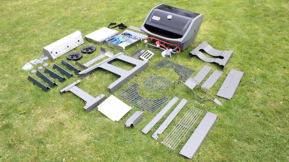 The parts of the Weber Spirit II E-310  laid out on a lawn, ready to be assembled