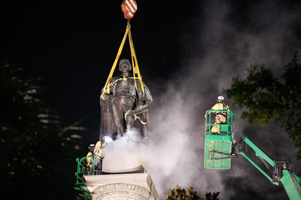 A worker uses a saw at the foot of the statue of John C. Calhoun atop a monument in his honor at Marion Square on June 24, 2020, in Charleston, S. C. Work crews began dismantling the monument in Tuesday evening.