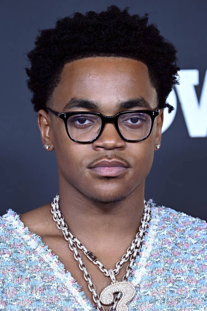 Michael Rainey Jr. at an event, wearing glasses, a textured shirt, and layered chain necklaces