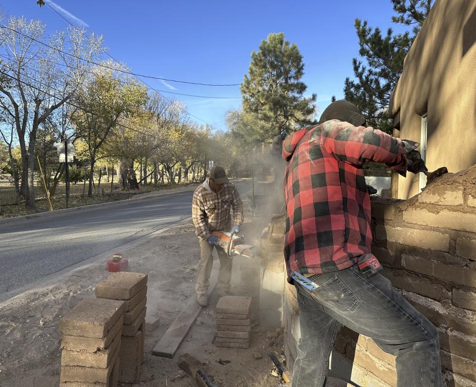 Masons works on an adobe-brick wall along a residential lane lined with multimillion-dollar homes in Santa Fe, N.M., on Friday, Nov. 3, 2023. Voters are deciding whether to tax mansions to pay for affordable housing initiatives in a state capital city prized for its desert-mountain vistas, vibrant arts scene and stucco architecture rooted in Native American and Spanish-colonial tradition. (AP Photo/Morgan Lee)