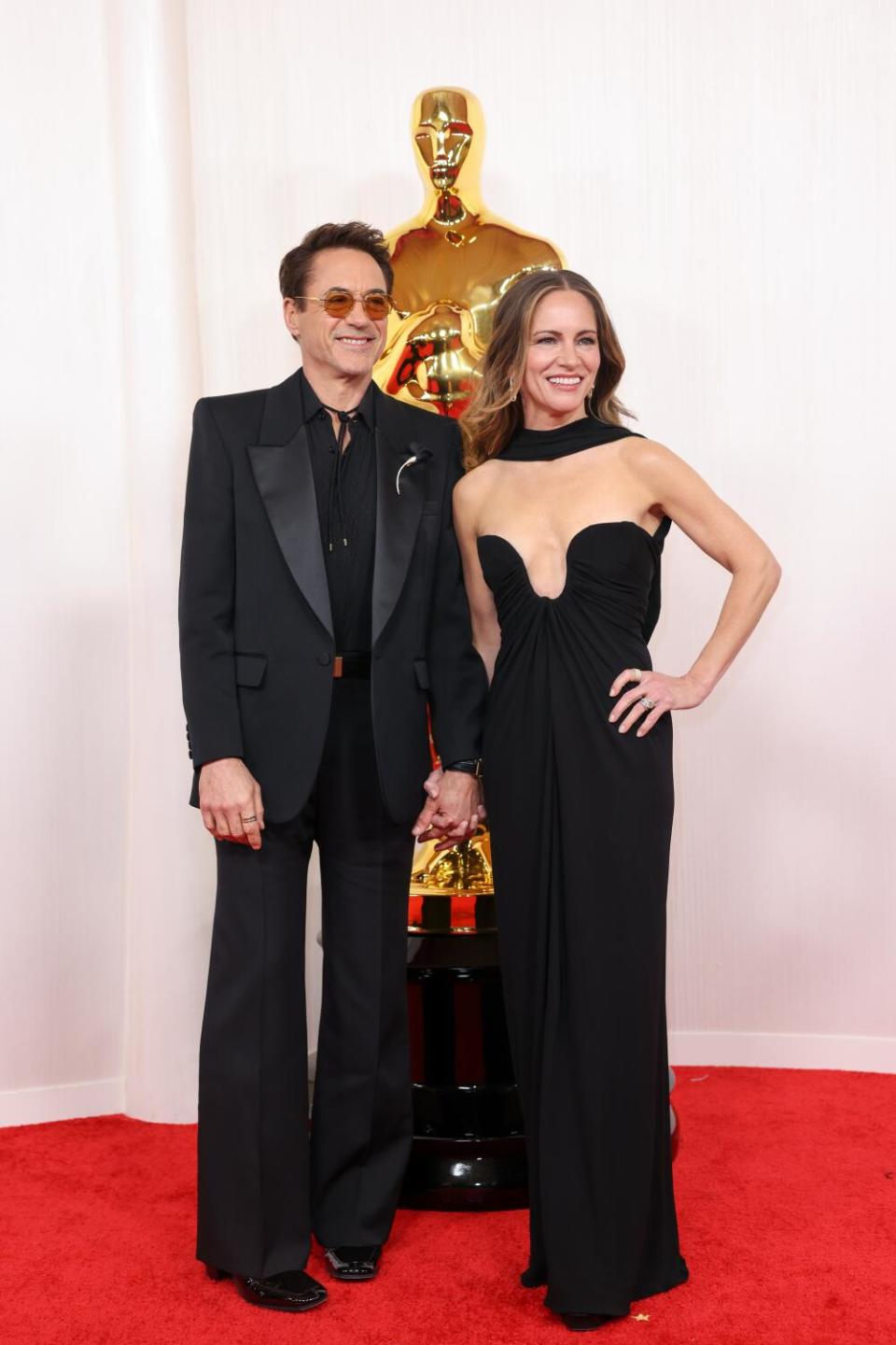 Robert Downey Jr. and Susan Downey, in black, stand in front of an Oscar statue.