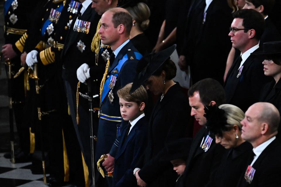 喬治王子（中）與父母站在一起，表情看起來很悲傷，也有民眾捕捉到他拭淚畫面。（AFP）