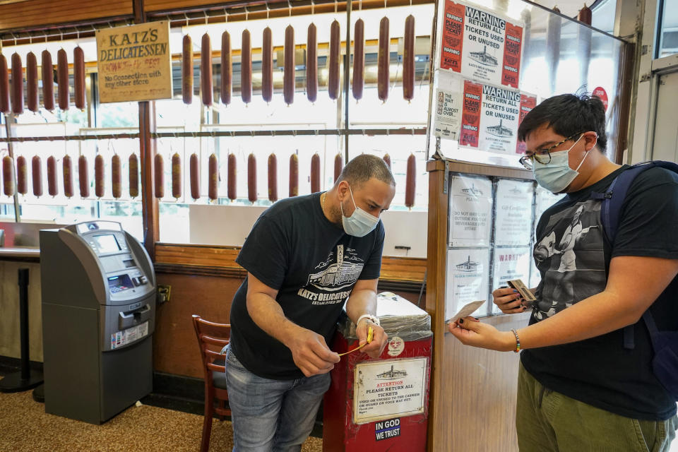 FILE — In this Aug. 17, 2021 file photo, a Katz's Deli employee, left, checks the proof of vaccination from a customer who will be eating inside the restaurant, in New York. Ticket agents dutifully ascertain the vaccination status of everyone passing through the turnstile at pro sports venues in some cities from Seattle and New York, and restaurant hosts do the same in many places. (AP Photo/Mary Altaffer, File)