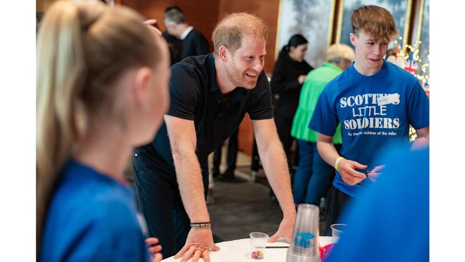 Prince Harry leaning on a table with a group of young people in blue shirts