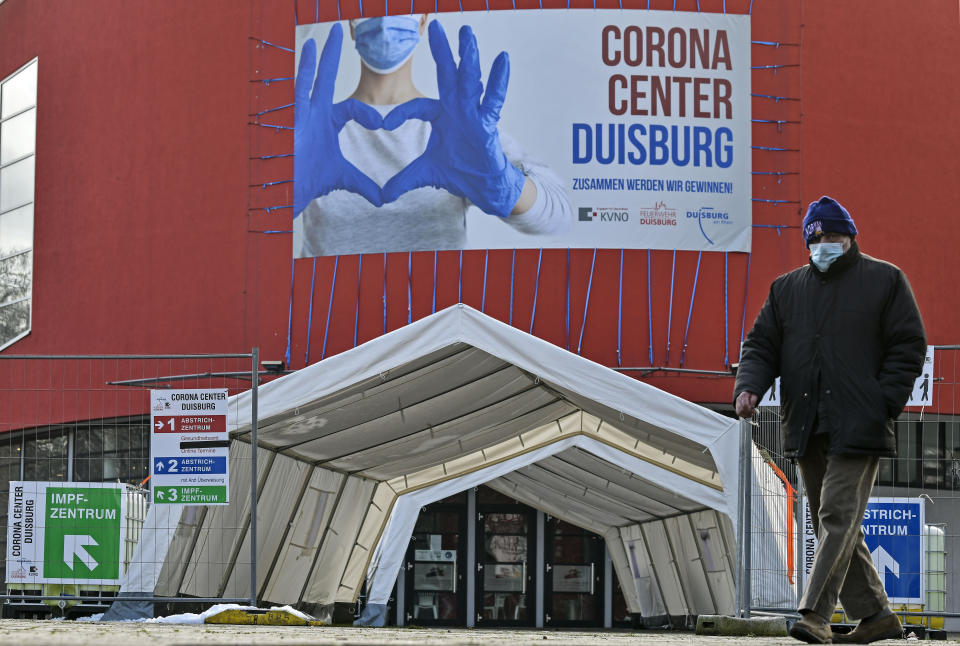 FILE - In this Monday, Jan. 25, 2021 file photo, a man wearing a face mask walks past the Corona Center in Duisburg, Germany. The former Musical theater has been turned into a COVID-19 test and vaccination center. With accusations of being slow off the blocks in the race to immunise its citizens against COVID-19, Germany faces the problem of having a glut of vaccines and not enough arms to inject. With its national vaccine campaign lagging far behind that of Israel, Britain and the United States, there are growing calls in this country of 83 million to ditch or rewrite the rulebook. (AP Photo/Martin Meissner, File)