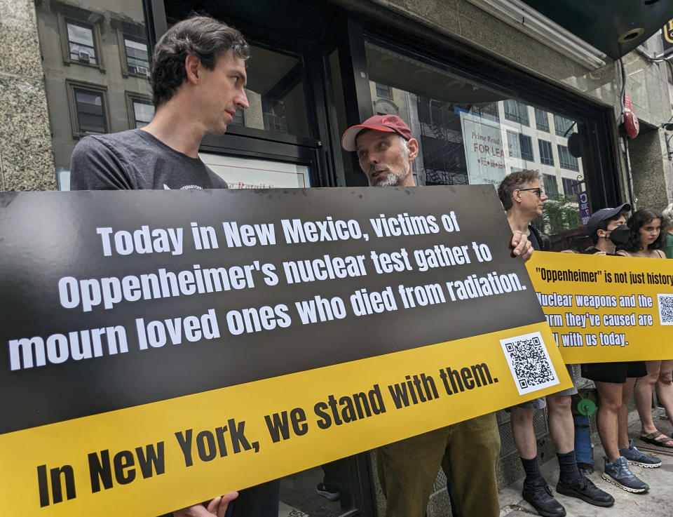 Matthew Bolton, a la izquierda, y Jan-Christoph Zoels, al centro, sostienen un cartel mientras se manifiestan en la ciudad de Nueva York el 15 de julio de 2023. Activistas se reunieron para llamar la atención hacia los residentes de Nuevo México que estuvieron expuestos a la radiación durante la prueba atómica Trinity realizada en 1945 como parte del Proyecto Manhattan. El mitin procedió a una proyección y un panel de discusión sobre la nueva película "Oppenheimer". (Andrew Facini vía AP)