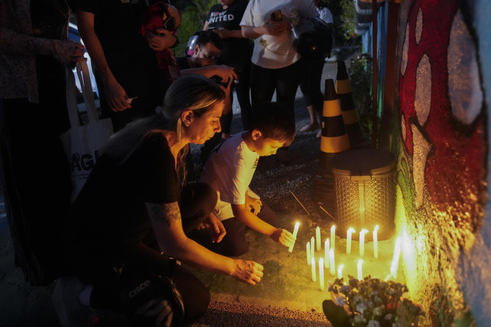 People place lit candles outside the "Cantinho do Bom Pastor" daycare center after a fatal attack on children in Blumenau, Brazil, Wednesday, April 5, 2023. A man with a hatchet jumped over a wall and burst into a day care center Wednesday in Brazil, killing four children and wounding at least four others, authorities said.(AP Photo/Andre Penner)