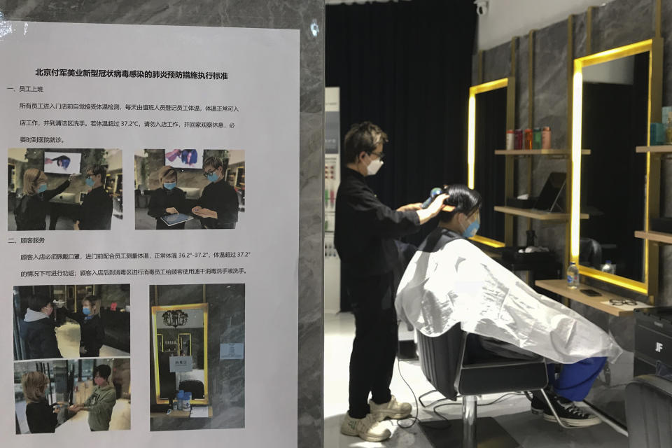 A barber cuts a client's hair near a disinfection notice at a hair salon in Beijing, Monday, Feb. 24, 2020. Monday is the second day of the second month of the Chinese lunar calendar, traditionally an auspicious time when people rush into barbershops to get new haircuts. Getting a fresh look on the day is thought to bring good luck for the year ahead, but getting a haircut has become a challenge in China now that most barbershops are temporarily shut to avoid public gatherings amid the virus outbreak. (AP Photo/Olivia Zhang)