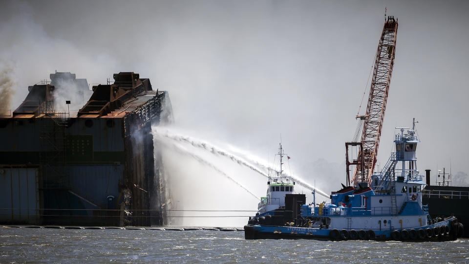 Firefighters working off two tug boats hose down the remains of the overturned cargo ship Golden Ray, Friday, May 14, 2021, Brunswick, Ga. The Golden Ray had roughly 4,200 vehicles in its cargo decks when it capsized off St. Simons Island south of Savannah on Sept. 8, 2019. (AP Photo/Stephen B. Morton)