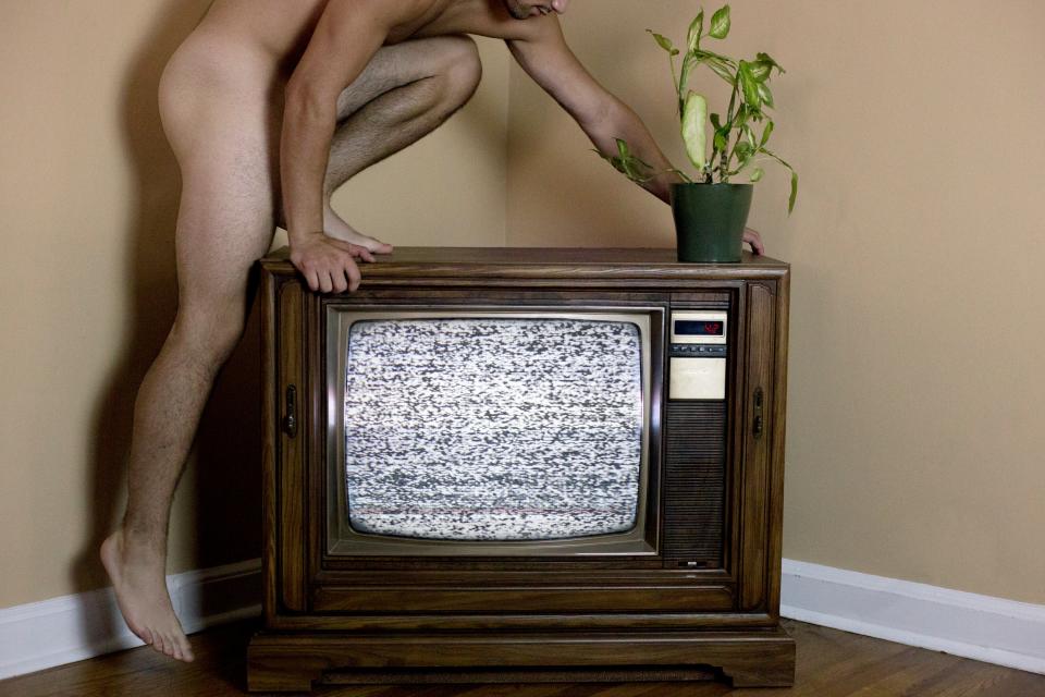 Photo of a nude man climbing onto an old television