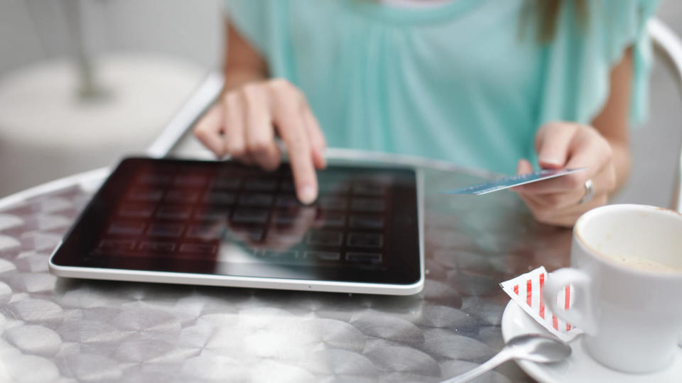 Woman does online shopping on tablet-PC with credit card while sitting in cafe.