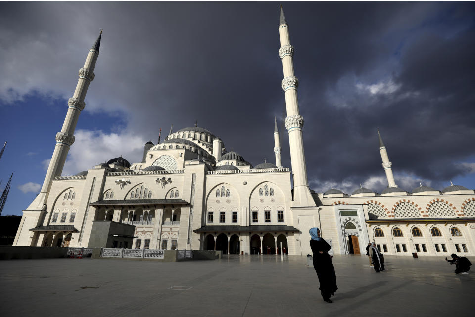 A woman walk as a man, right, takes photos at the Camlica mosque in Istanbul, Sunday, March 31, 2019. Turkish citizens have begun casting votes in municipal elections for mayors, local assembly representatives and neighborhood or village administrators that are seen as a barometer of Erdogan's popularity amid a sharp economic downturn. (AP Photo/Emrah Gurel)