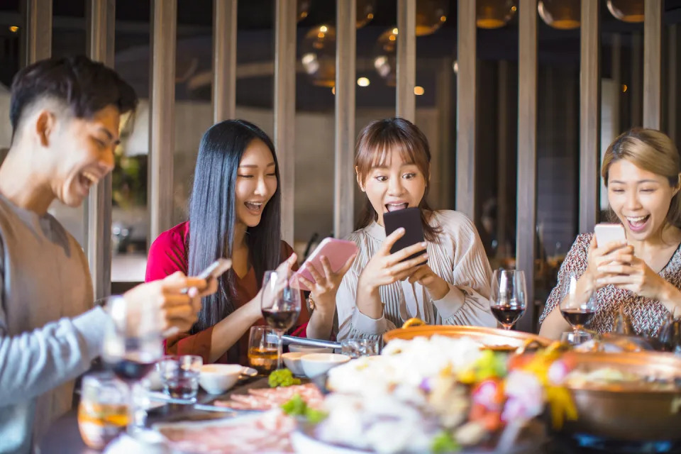 Group of friends eating and looking at smart phones (Photo: Getty Images)