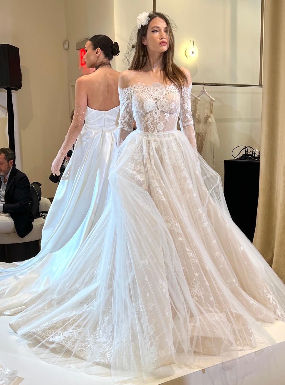 A woman poses in a wedding dress with a lace, sheer bodice and off-the-shoulder sleeves.