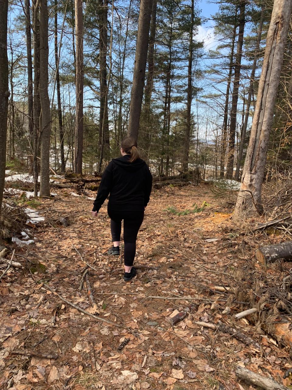 woman hiking in the vermont woods in a black outfit, facing the other way
