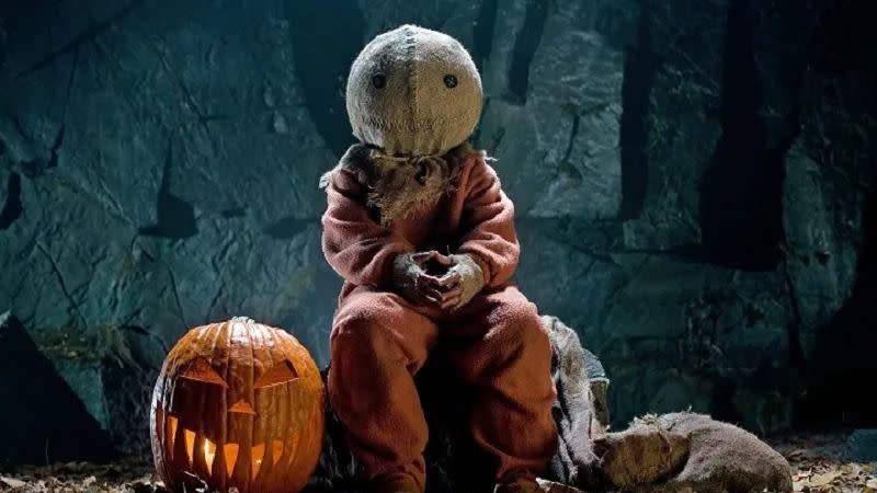 trick r treat sam wearing a burlap mask sits with a pumpkin in a scene from trick r treat a good housekeeping pick for best halloween movies