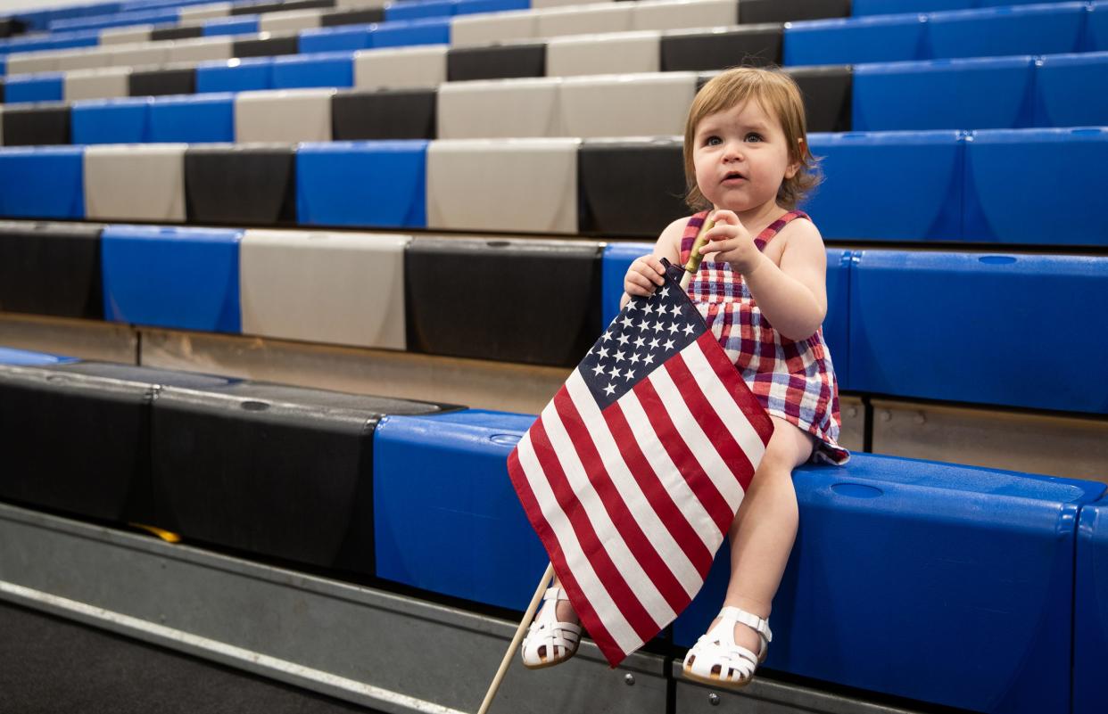 Laila Yassine, 17 months, sits on bleachers while holding an American flag during a naturalization ceremony at South Mountain Community College in Phoenix on Tuesday, July 4, 2023.